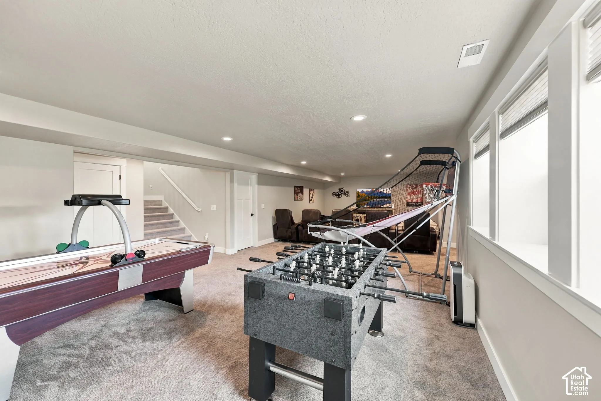 Spacious finished lower level with recessed lighting, light-colored carpeting, multiple windows, and a staircase