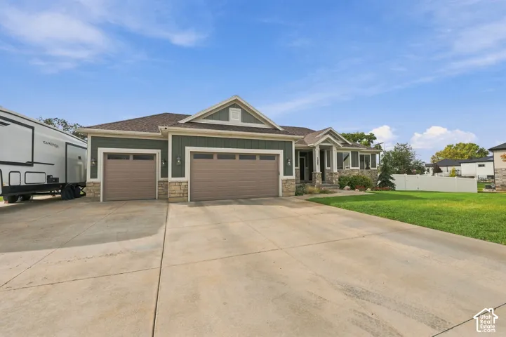 Exterior featuring green siding, stone accents, a multi-car garage, and a concrete driveway
