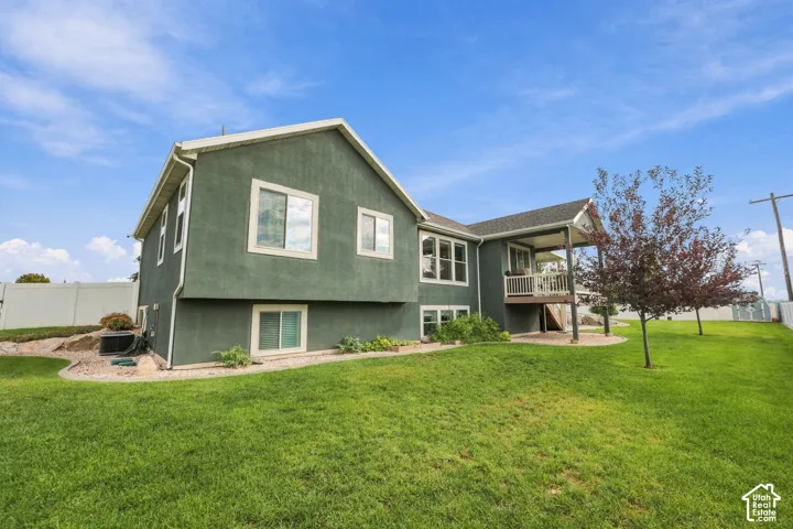 Stucco exterior with white trim, covered deck with white railings, multiple windows, and a landscaped yard
