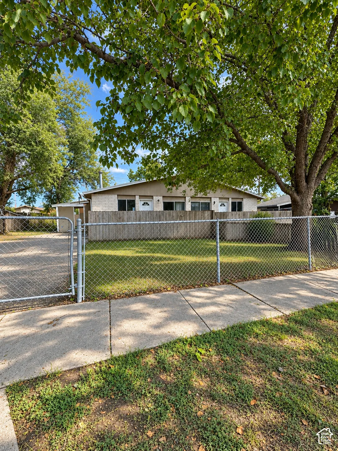 Chain-link fencing encompasses the property, featuring a concrete sidewalk and a paved driveway