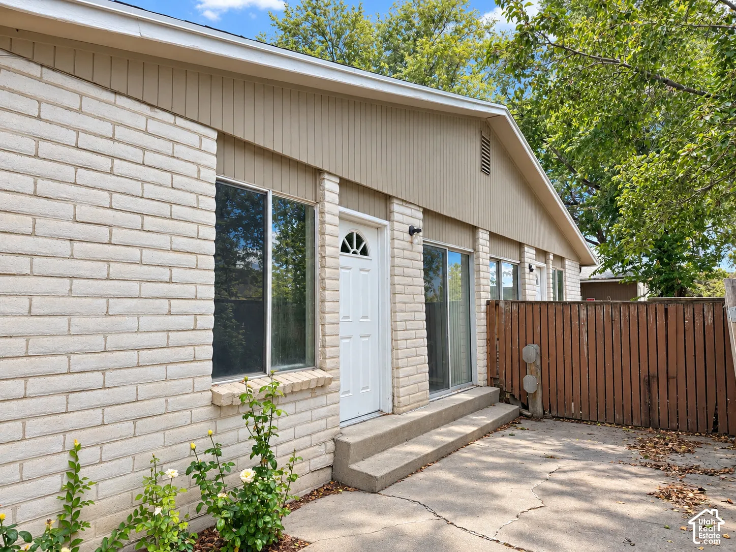 Brick exterior with vertical siding accents, multiple windows, and a wood privacy fence