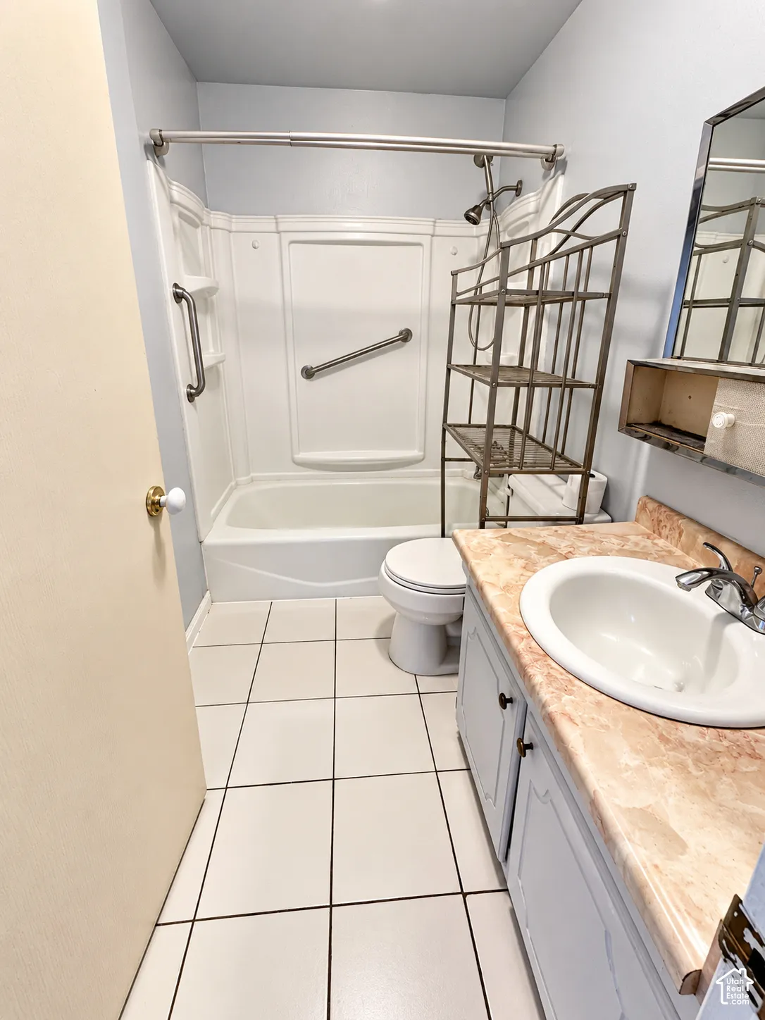 Tile flooring, vanity with integrated sink, shower-tub combination, wall-mounted mirror, and cabinet storage
