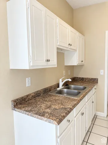 White shaker-style cabinetry with chrome hardware, dual-basin stainless steel sink, speckled laminate countertops, and tile flooring