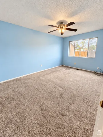 Expansive room featuring light blue walls, brown carpet, and a ceiling fan with integrated lighting