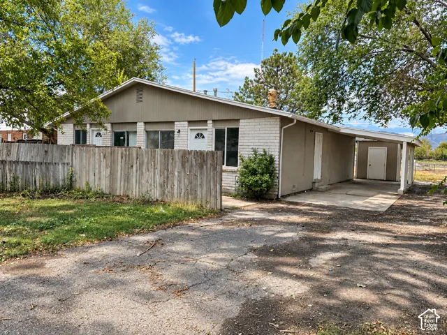 Brick and painted wood exterior with multiple entry doors, covered carport, and a separate storage shed