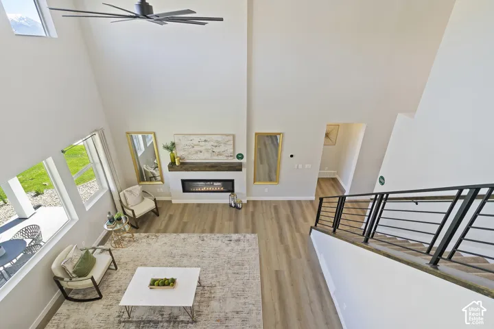 Vaulted ceiling with a contemporary ceiling fan, linear electric fireplace with wood mantel, multiple large windows, wood-finish flooring, and a modern staircase with metal railings