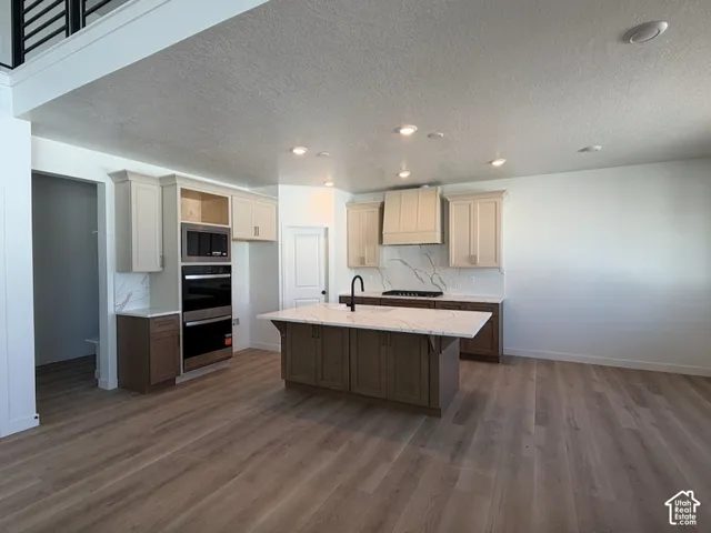 Open-concept kitchen with wood-finish flooring, recessed lighting, double wall ovens, a large island with a countertop, and a built-in microwave