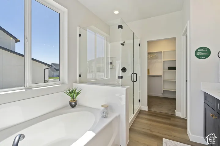 Soaking tub with a matte black faucet, glass-enclosed shower with matte black fixtures, wood-finish flooring, and a walk-in closet with built-in shelving