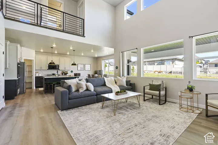 Open-concept living area with soaring ceilings, wood-finish flooring, a kitchen island, and a second-story interior balcony with black metal railings