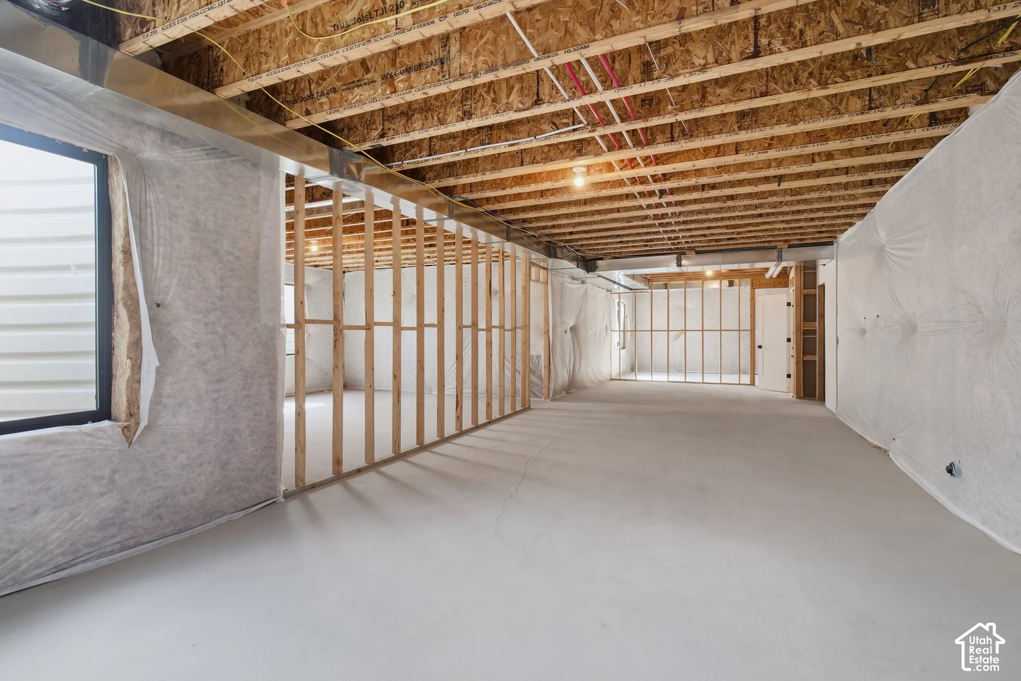 Unfinished basement featuring exposed wood joists, concrete flooring, framed wall structures, and a window opening