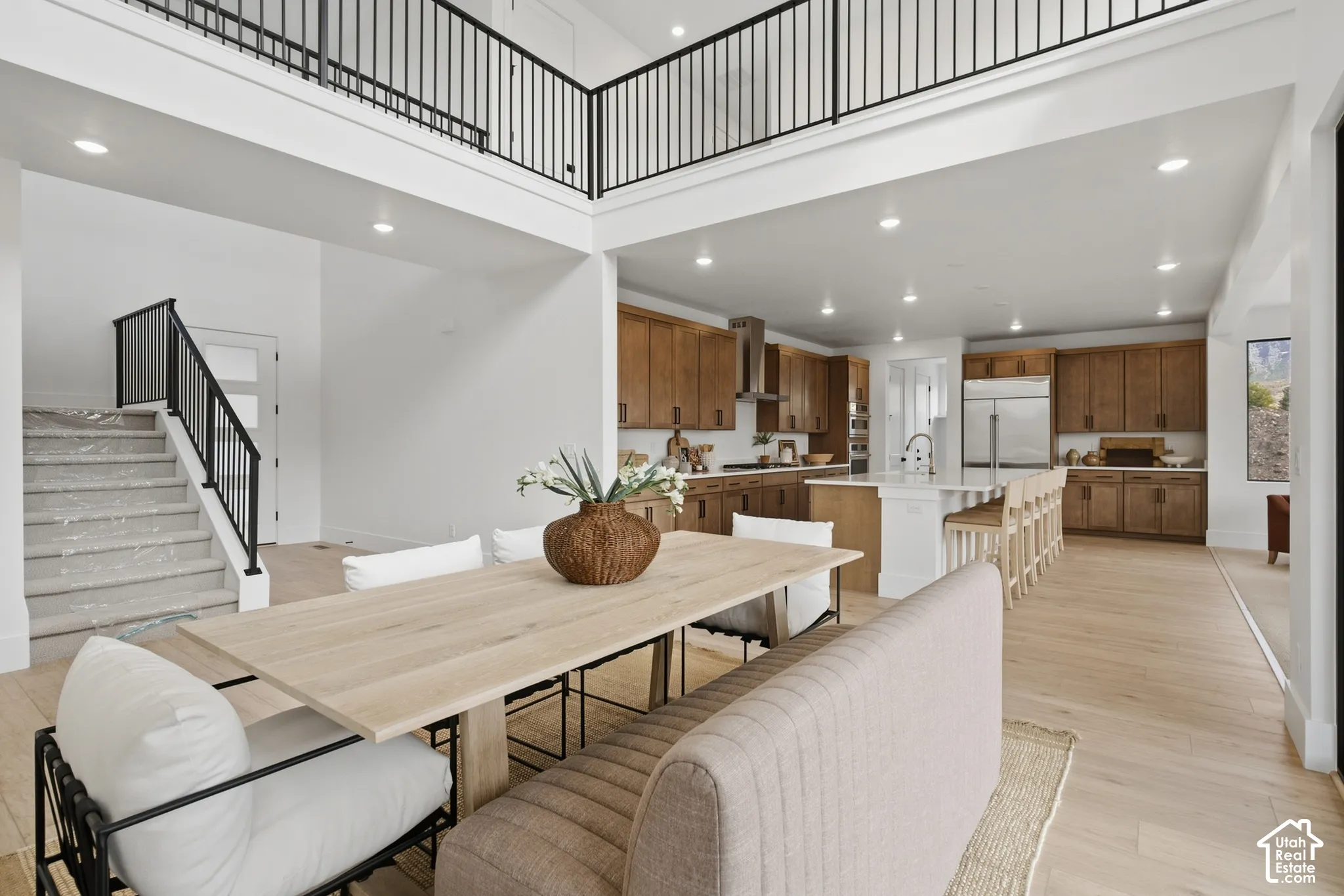 Open-concept living space with light wood-finish flooring, a kitchen featuring wood cabinetry and stainless steel appliances, and a central kitchen island with seating