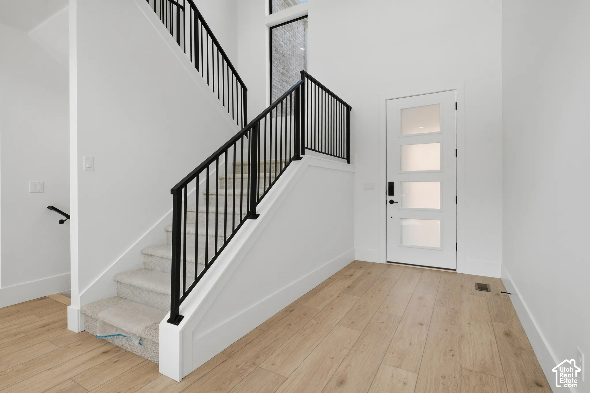 Two-story entryway featuring light wood-finish flooring, a contemporary staircase with black metal balusters, and a modern entry door with frosted glass panels