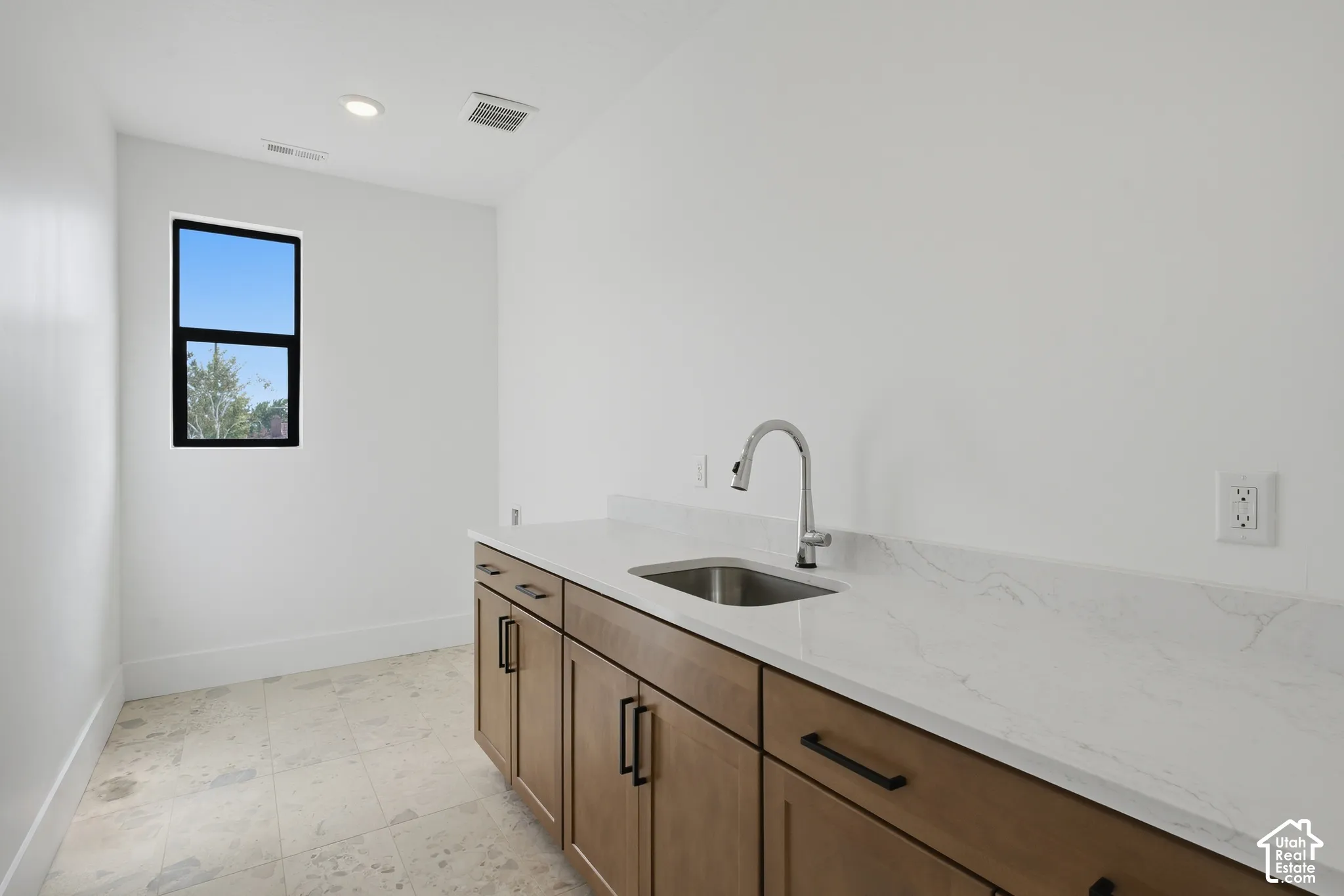 Light-toned wood cabinetry with matte black hardware, stainless steel sink, and light-toned stone countertop