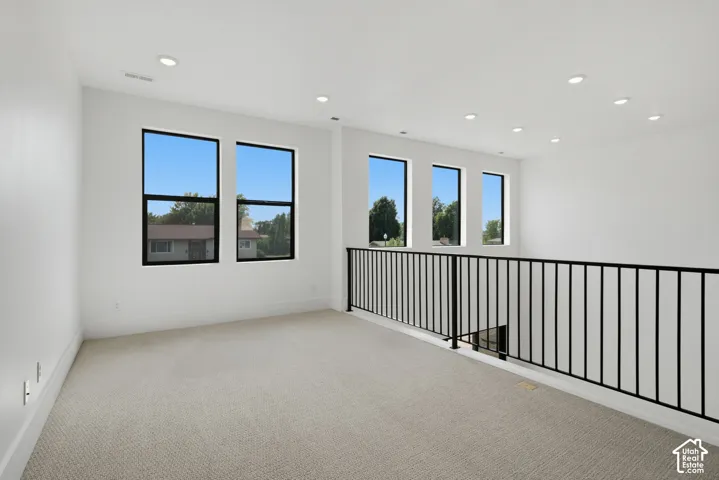 Loft area featuring neutral carpet and a black metal railing