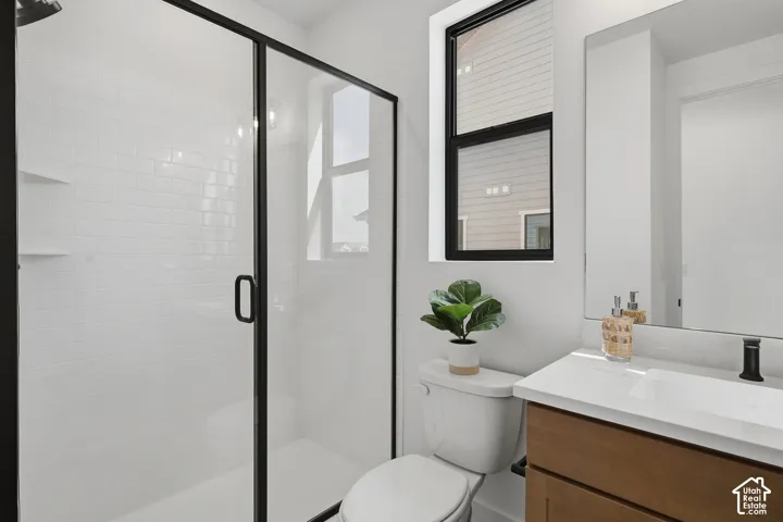 Walk-in shower with subway tile surround, clear glass enclosure with black framing, wood-finish vanity with white countertop, and black-framed window