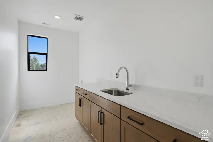 Light-toned wood cabinetry with matte black hardware, stainless steel sink, and light-toned stone countertop
