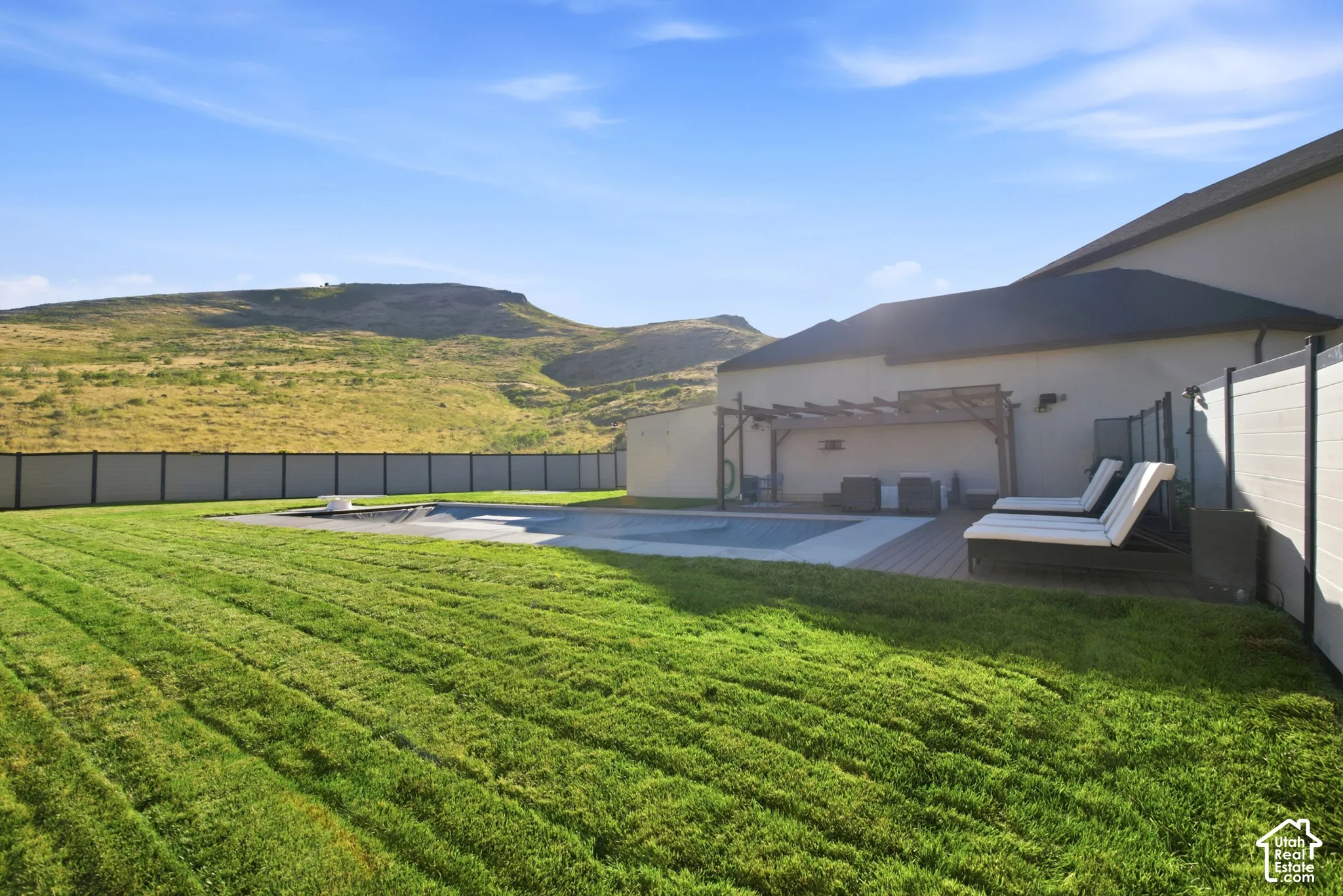 Expansive backyard with a covered pool, surrounding wood-finish decking, and a slatted pergola