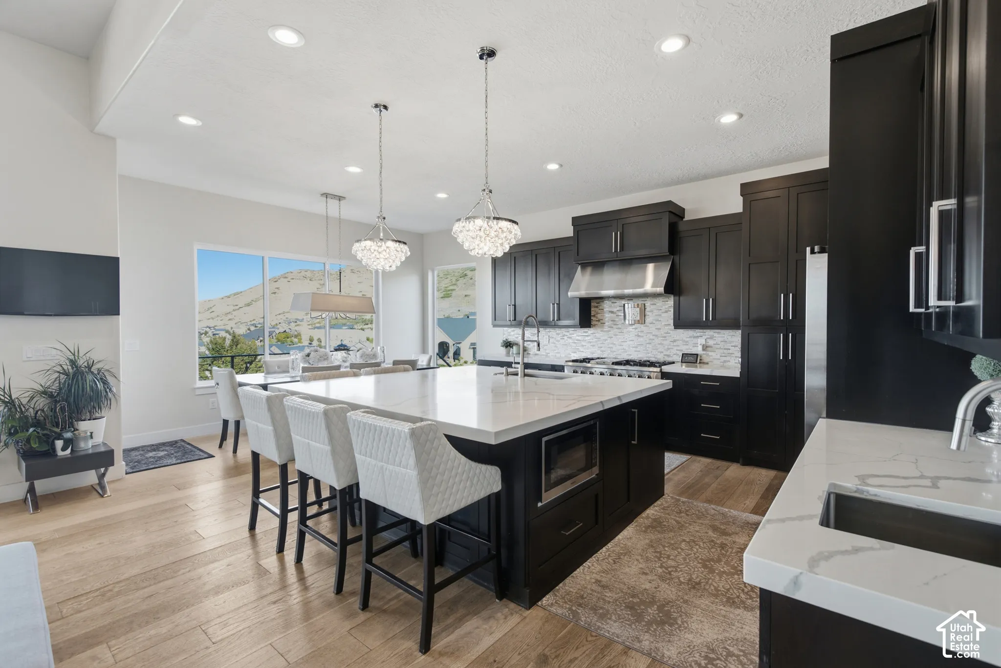 Gourmet kitchen featuring dark wood cabinetry, stainless steel appliances, a white quartz island with seating, pendant lighting, and wood-finish flooring