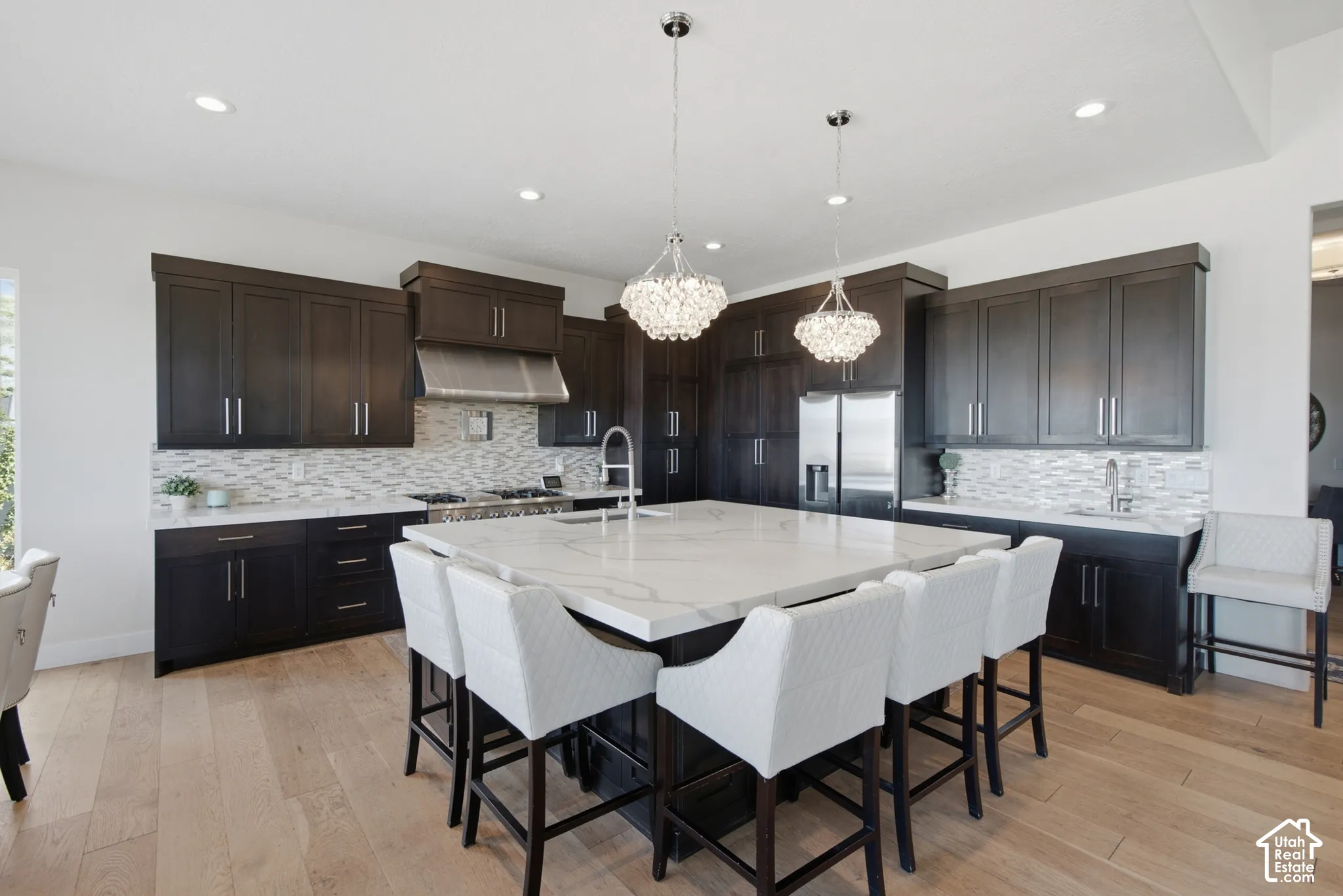 Expansive kitchen featuring dark wood cabinetry, light wood-finish flooring, a large center island with a white countertop, and stainless steel appliances