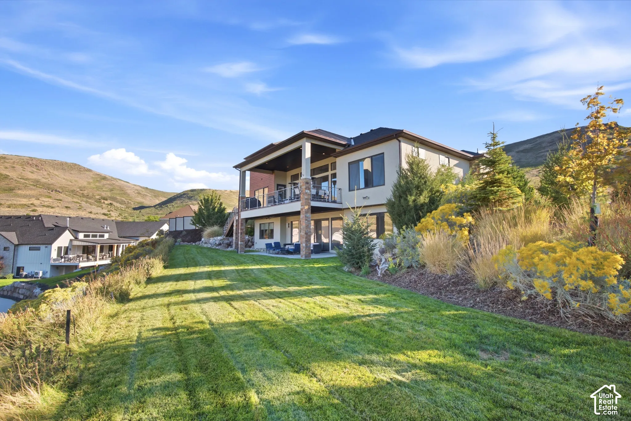 Expansive terraced yard with a manicured lawn, established landscaping, and a multi-level deck and patio