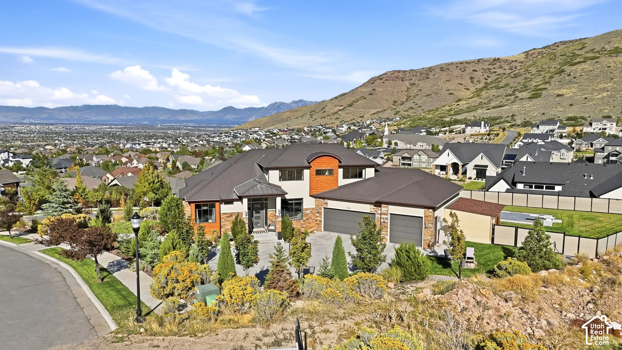 Multi-level residence featuring a two-car garage, stone and wood-finish siding, extensive landscaping, and a manicured lawn