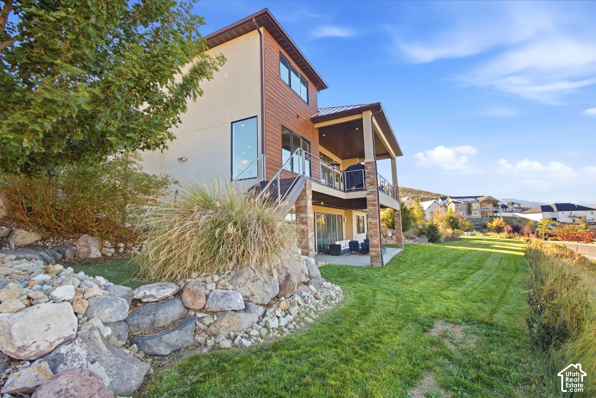 Multi-level exterior with a covered upper balcony, ground-level patio, and a stone-accented facade