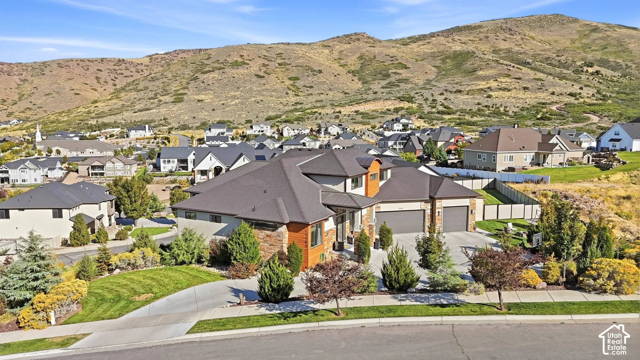 Stone and wood-tone exterior with dark roofline, an attached two-car garage, and established landscaping