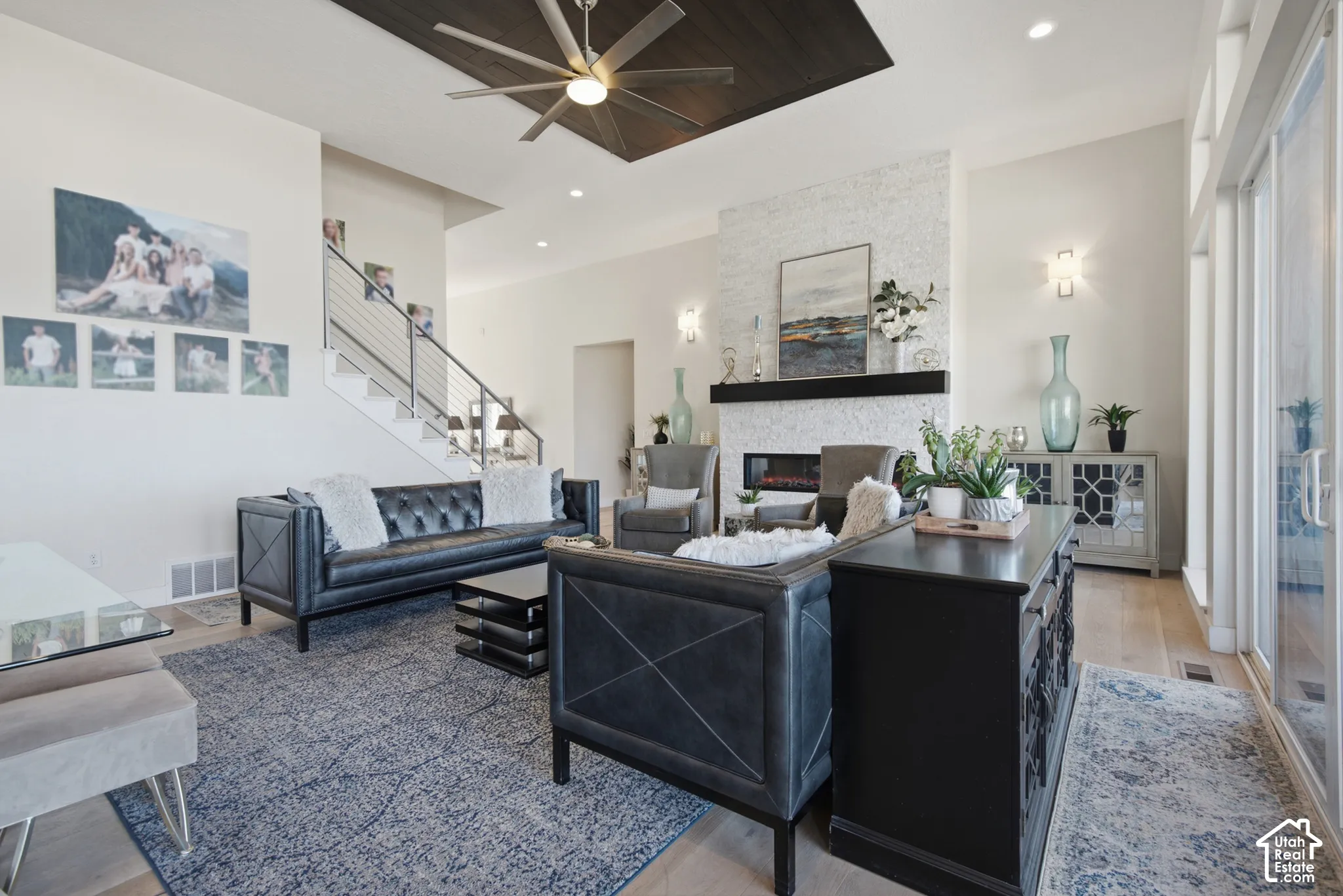 Spacious living area featuring light wood-finish flooring, a contemporary fireplace with a decorative tile surround, and a ceiling fan with a dark wood-paneled accent