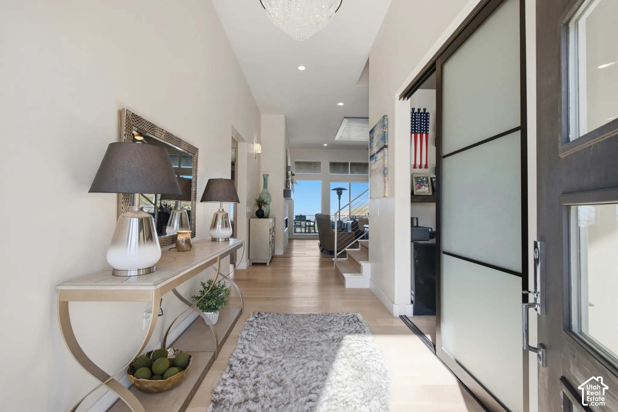 Spacious entryway featuring light wood-finish flooring, a contemporary chandelier, recessed lighting, a sliding frosted glass panel door, and an open concept layout