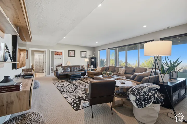 Recessed lighting, light-toned carpeting, wood-finish floating media console, and a wall of windows
