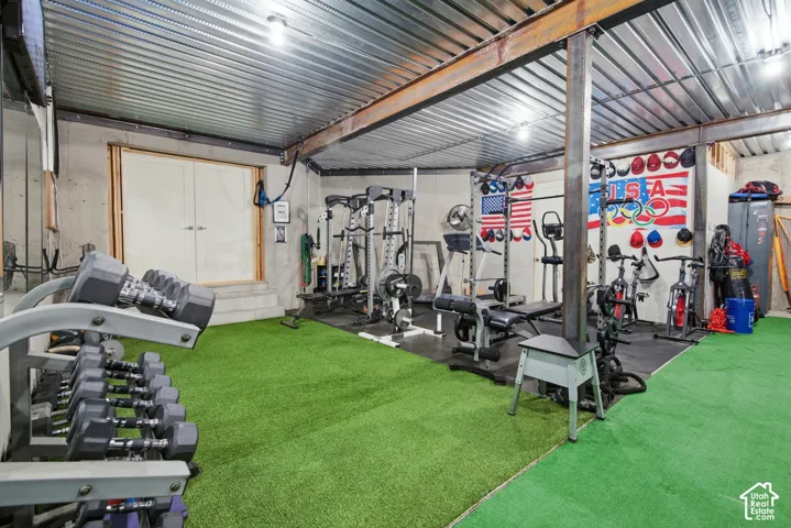 Concrete walls, corrugated metal ceiling, exposed structural beams, double doors, and turf flooring