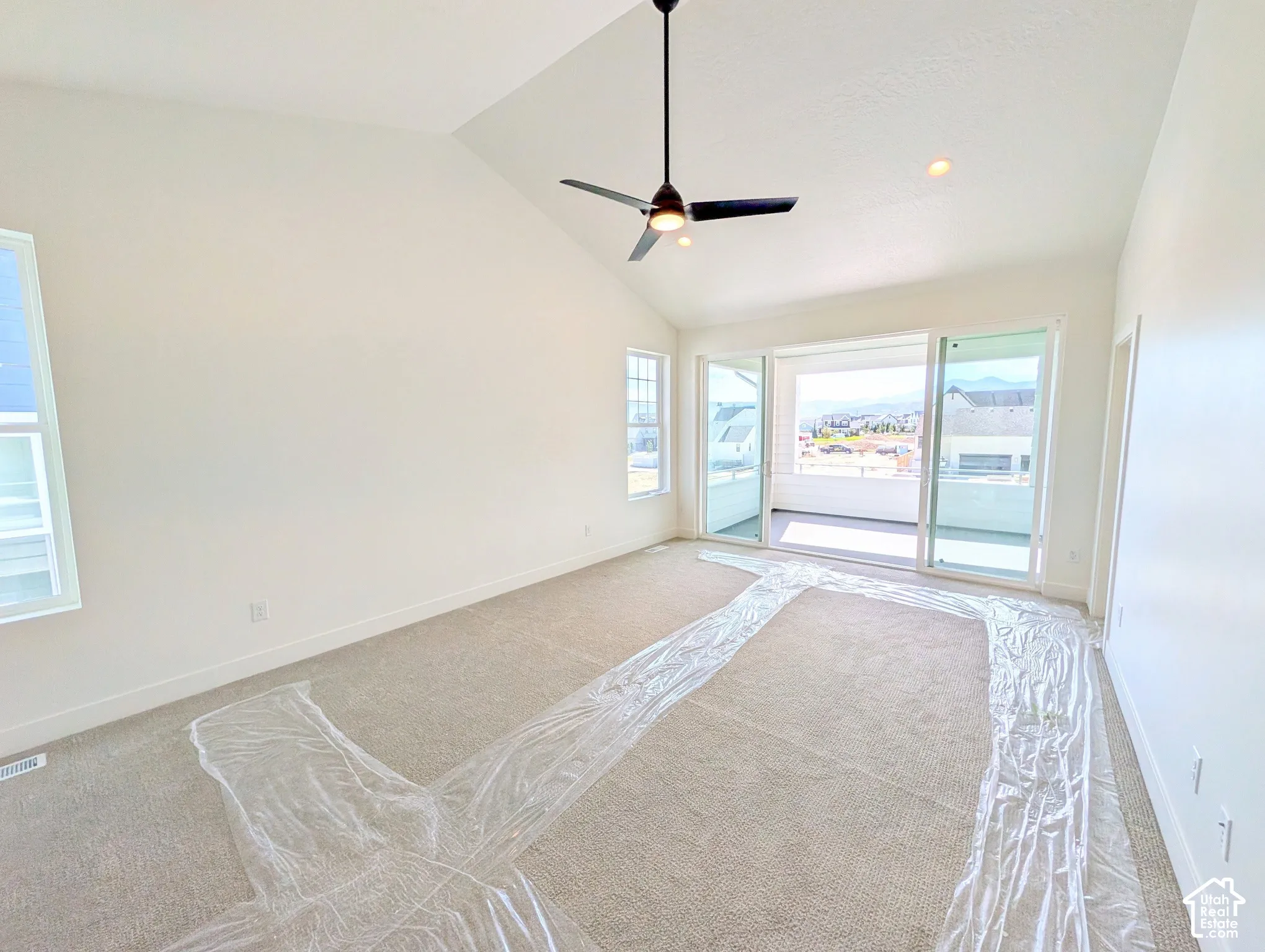 Primary bedroom with Vaulted ceiling, ceiling fan, recessed lighting, carpeted flooring, and sliding glass door access to a balcony