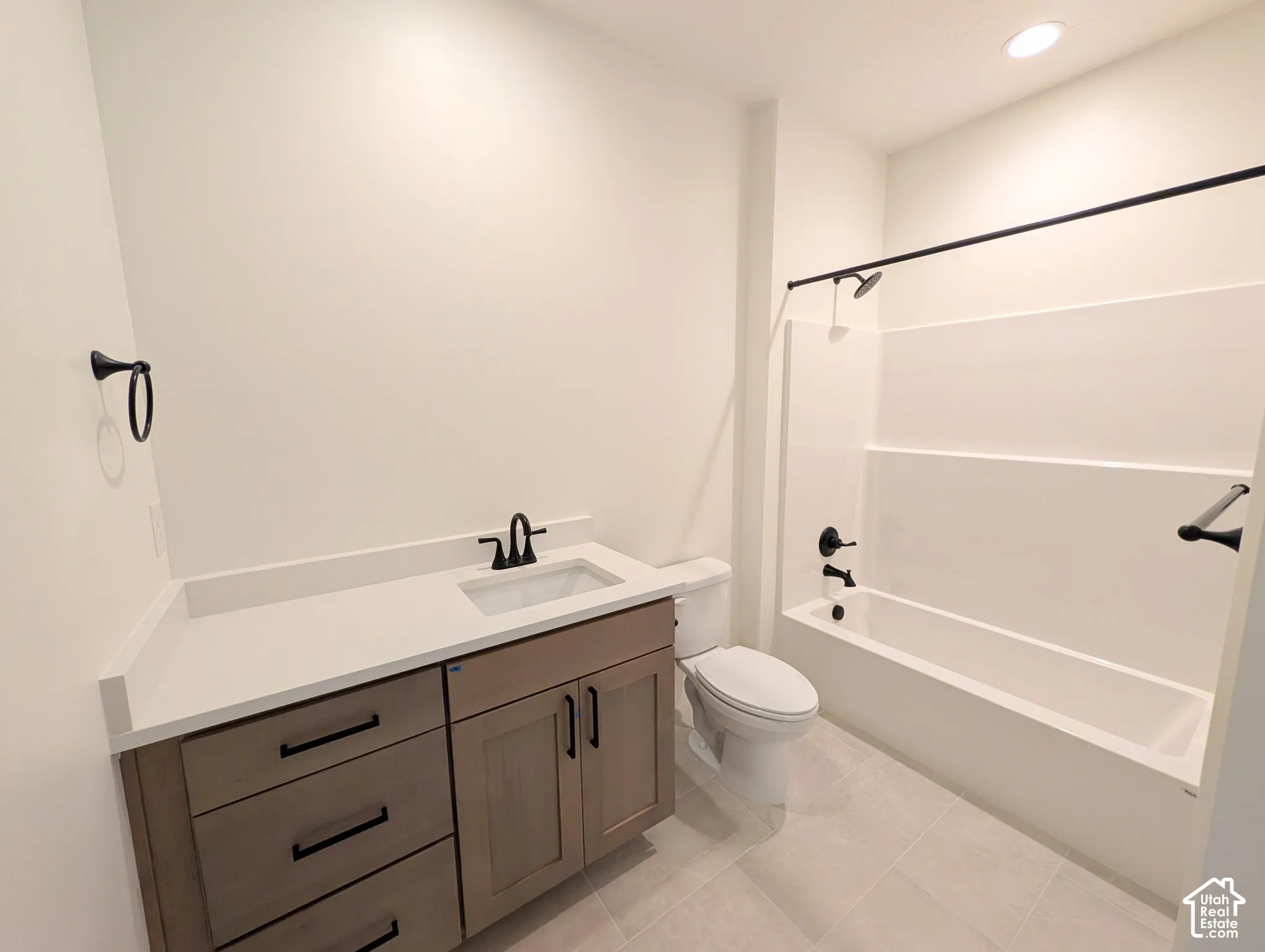 Contemporary bathroom featuring a wood-finish vanity with a light-colored countertop, recessed lighting, and a white tub and shower surround