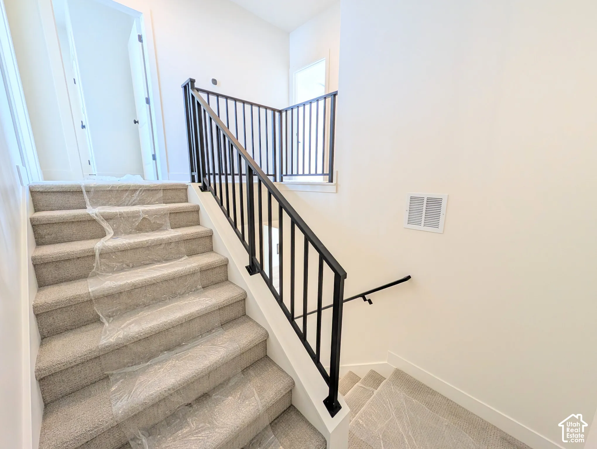 Carpeted staircase with black iron railings, white risers, and neutral wall tones
