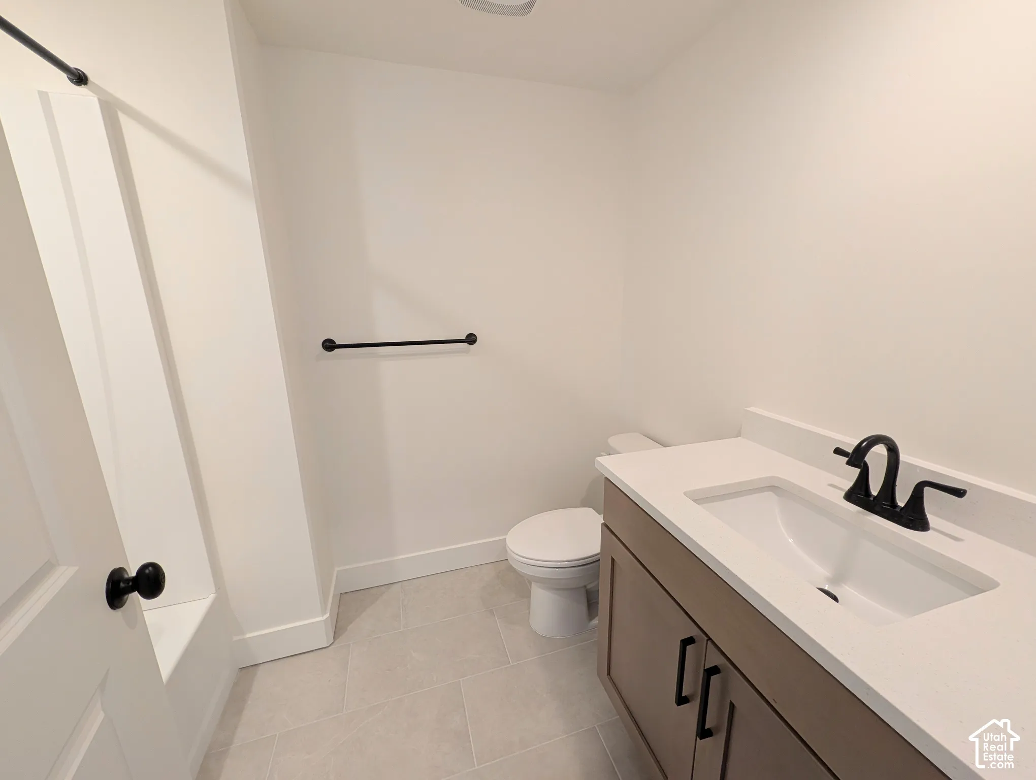 Contemporary bathroom featuring a wood-finish vanity with a white countertop and integrated sink, matte black faucet, and light-toned floor tiling