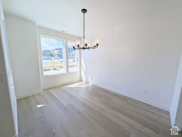 Spacious room featuring light wood-finish flooring, multiple windows, a modern chandelier with glass shades, and white painted walls