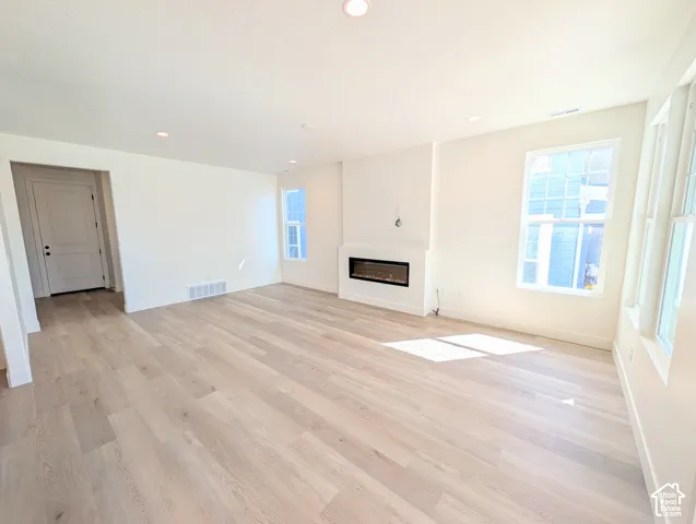 Spacious room featuring wood-finish flooring, an integrated electric fireplace, recessed lighting, and multiple windows