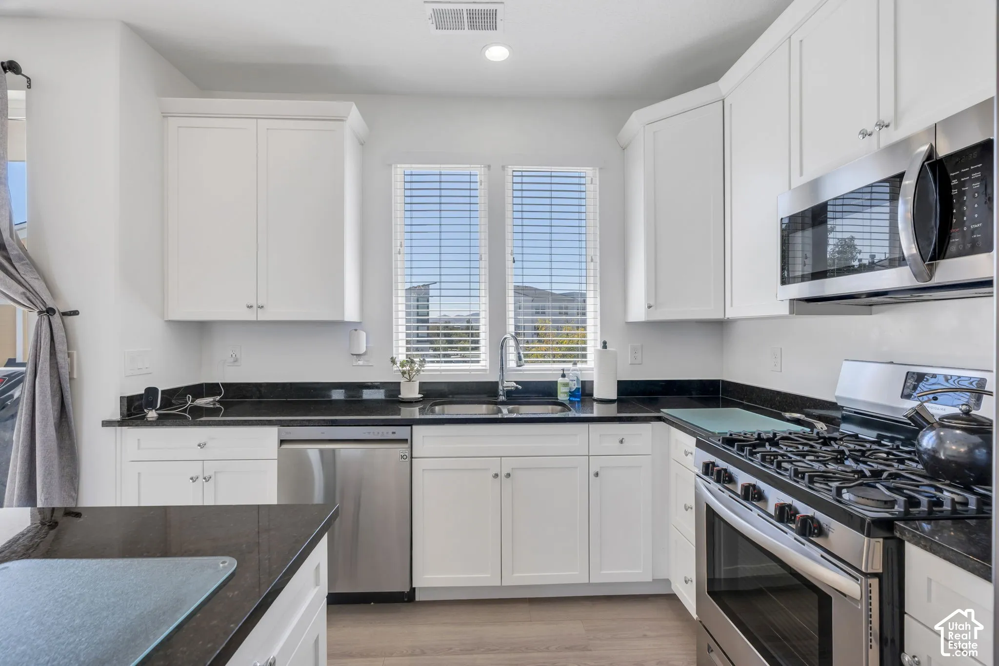White shaker-style cabinetry, black countertops, stainless steel appliances, and wood-finish flooring