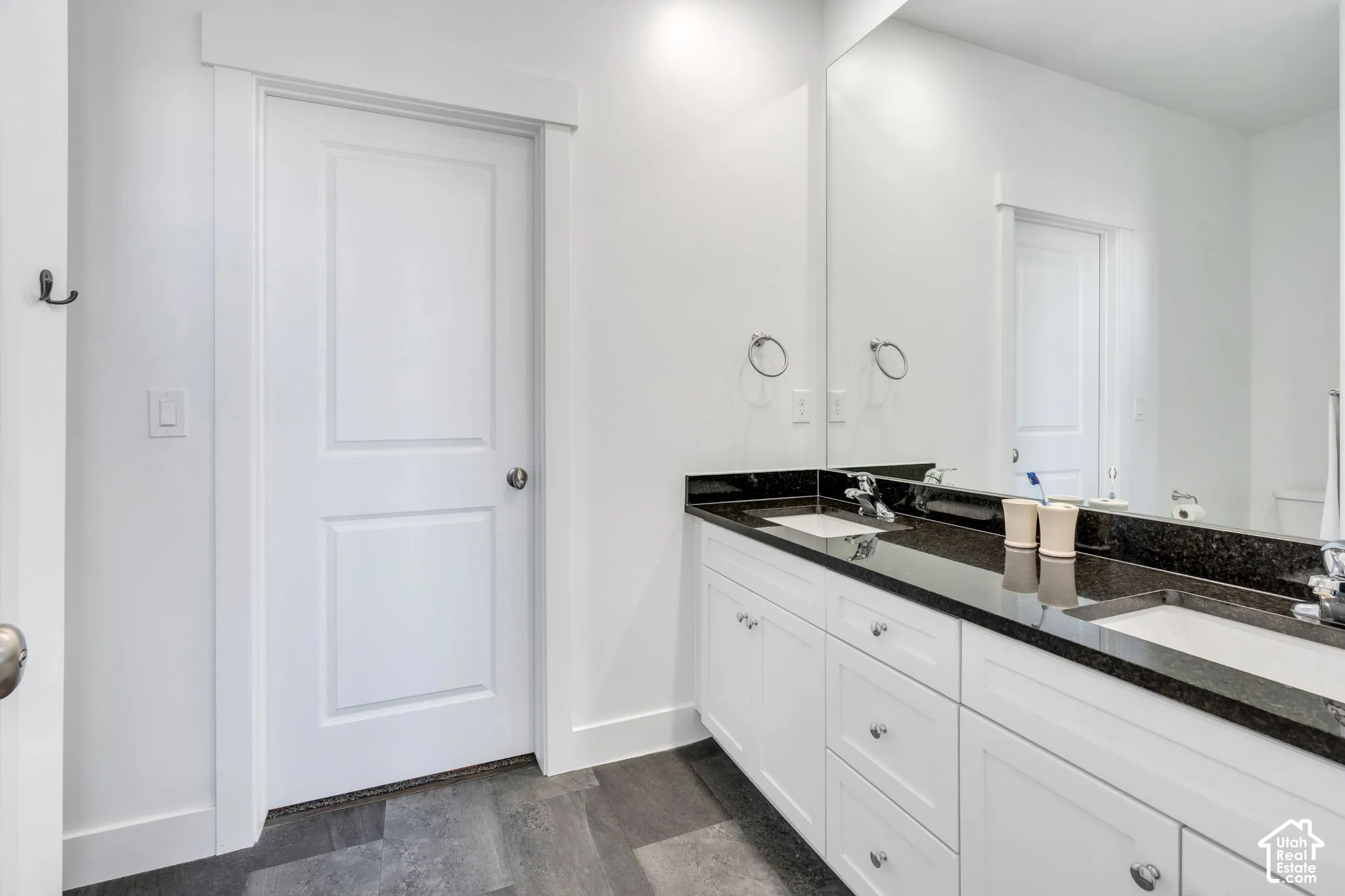 Double vanity with integrated sinks, dark stone countertop, white cabinetry, and wood-finish flooring
