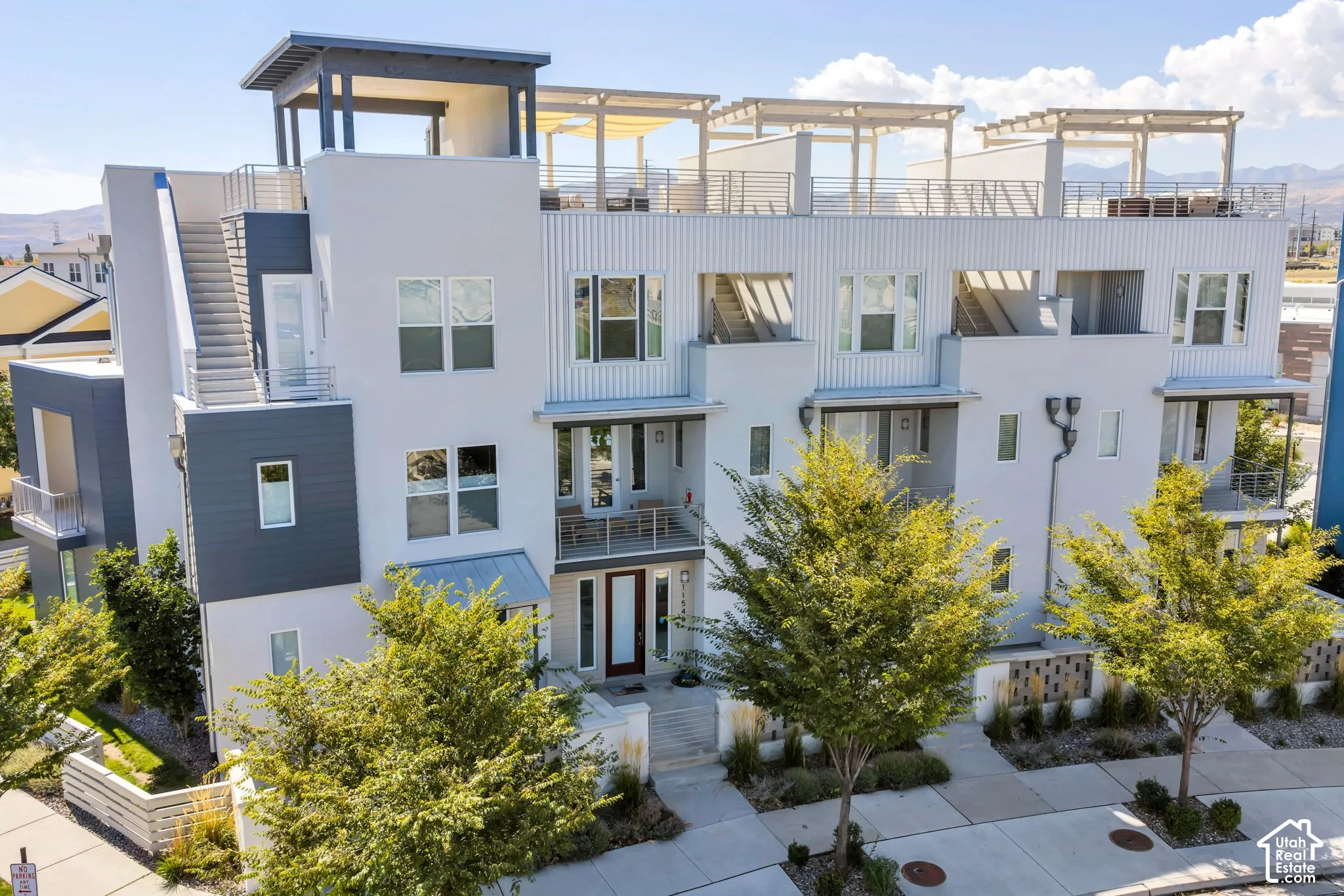 Modern multi-story facade featuring multiple balconies and a rooftop deck with pergola structures