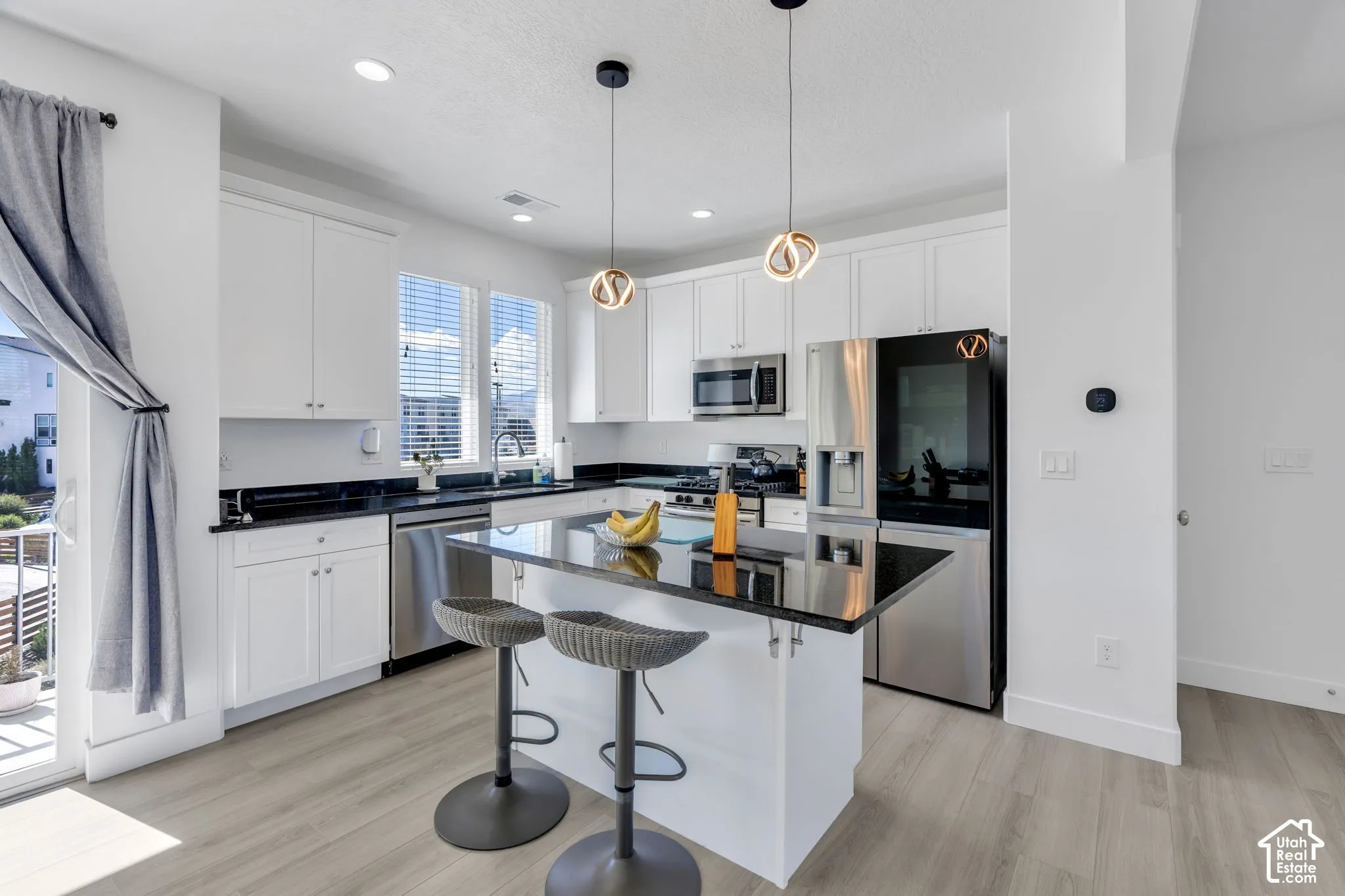 Modern kitchen featuring white cabinetry, black countertops, stainless steel appliances, a center island with seating, and light wood-finish flooring