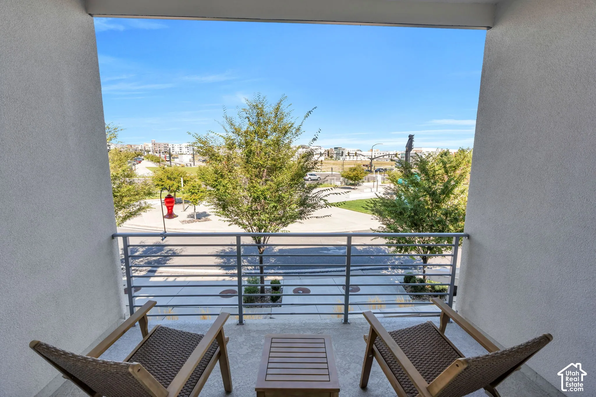Balcony with concrete flooring and horizontal metal railings overlooking a landscaped area with trees and paved surfaces