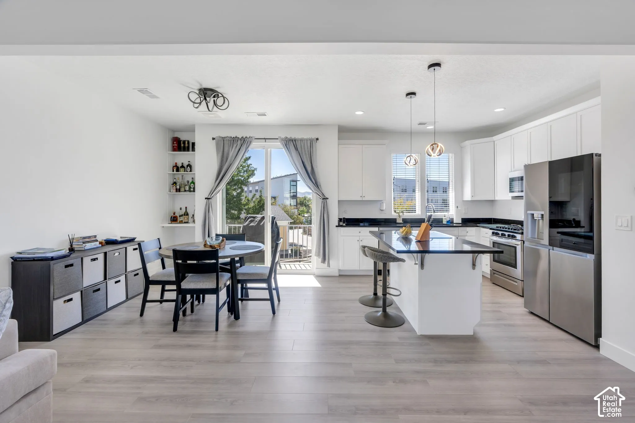 Open-concept living space with wood-finish flooring, white cabinetry, a kitchen island with seating, dark countertops, and stainless steel appliances