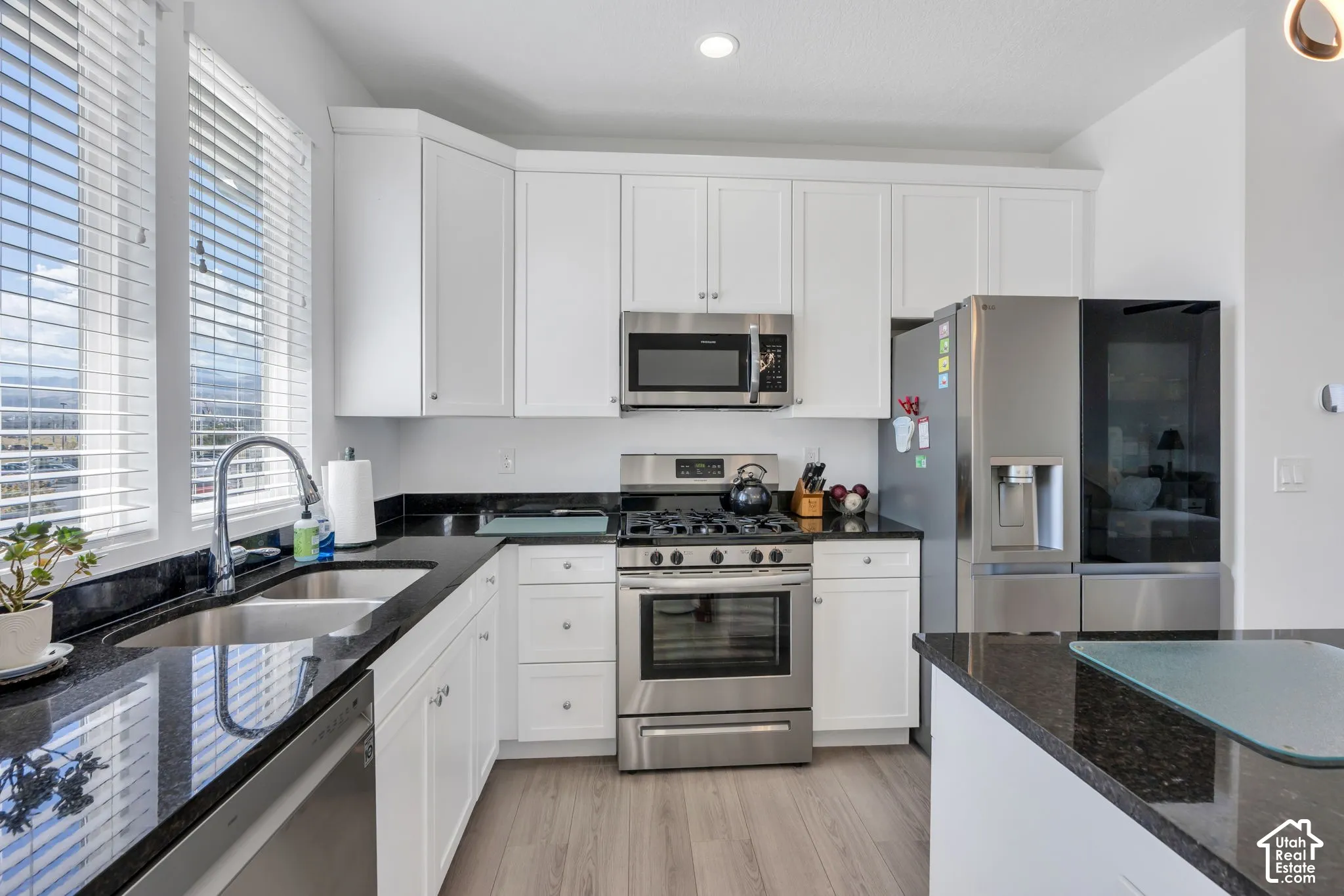 Kitchen featuring white cabinetry, dark stone countertops, stainless steel appliances, a stainless steel sink, and wood-finish flooring