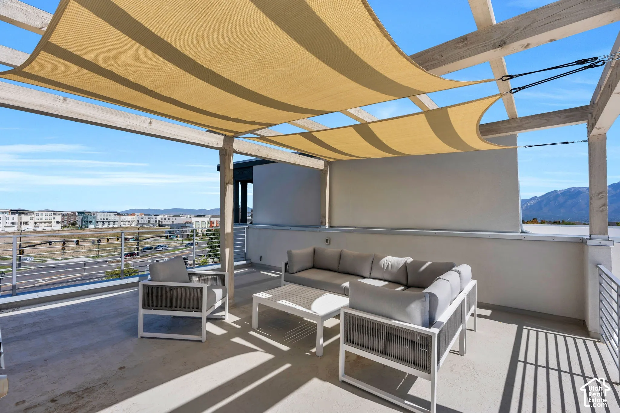 Rooftop patio featuring a slatted pergola with shade sails, a concrete surface, and a metal railing