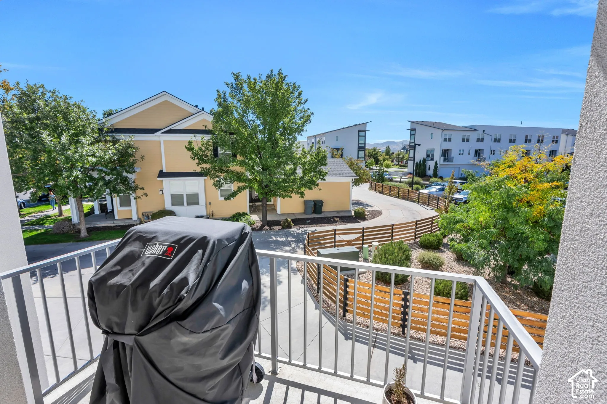 Balcony with metal railing overlooking landscaped grounds and residential buildings