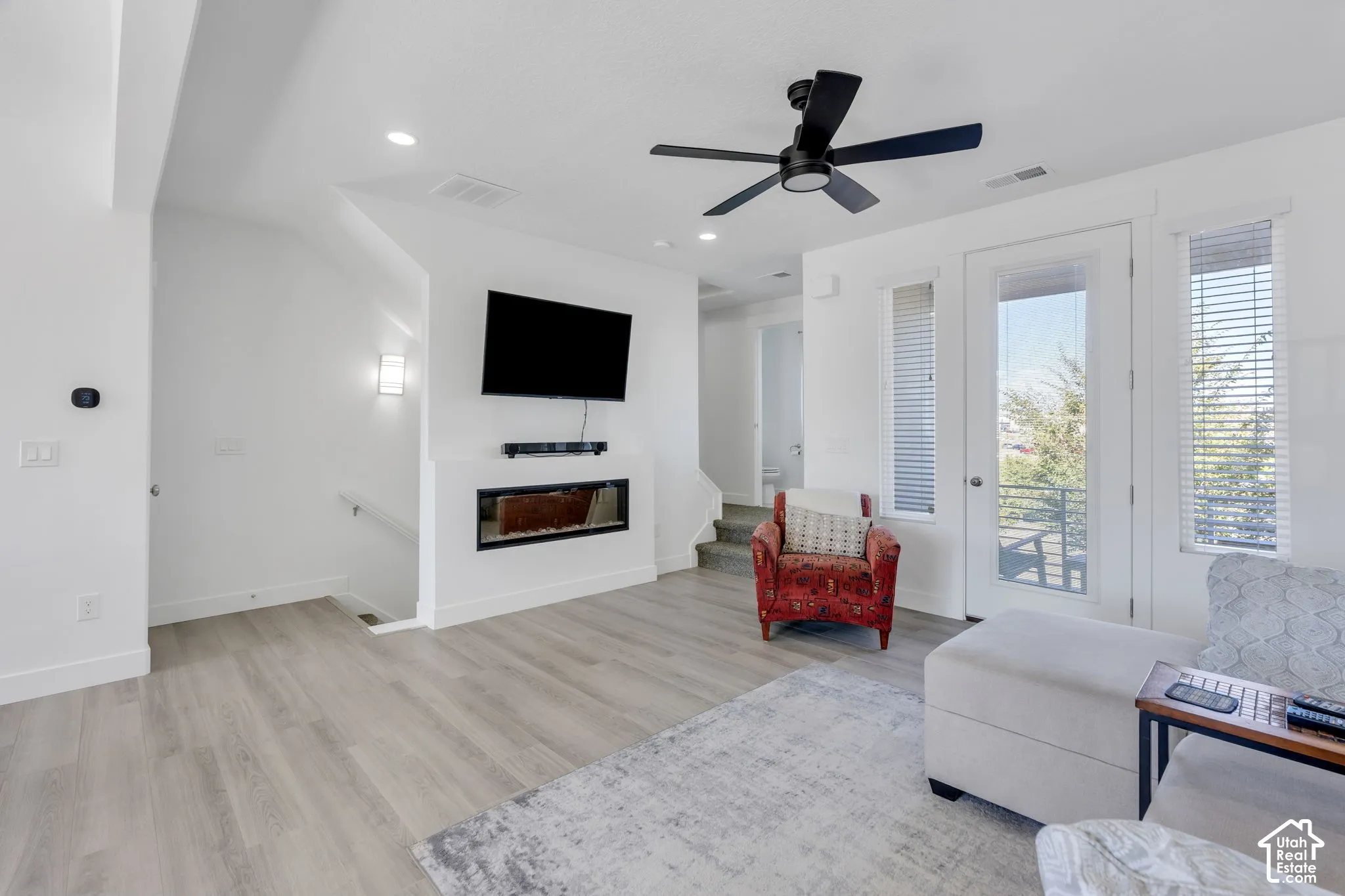 Modern living area with wood-finish flooring, a built-in electric fireplace, and a contemporary black ceiling fan