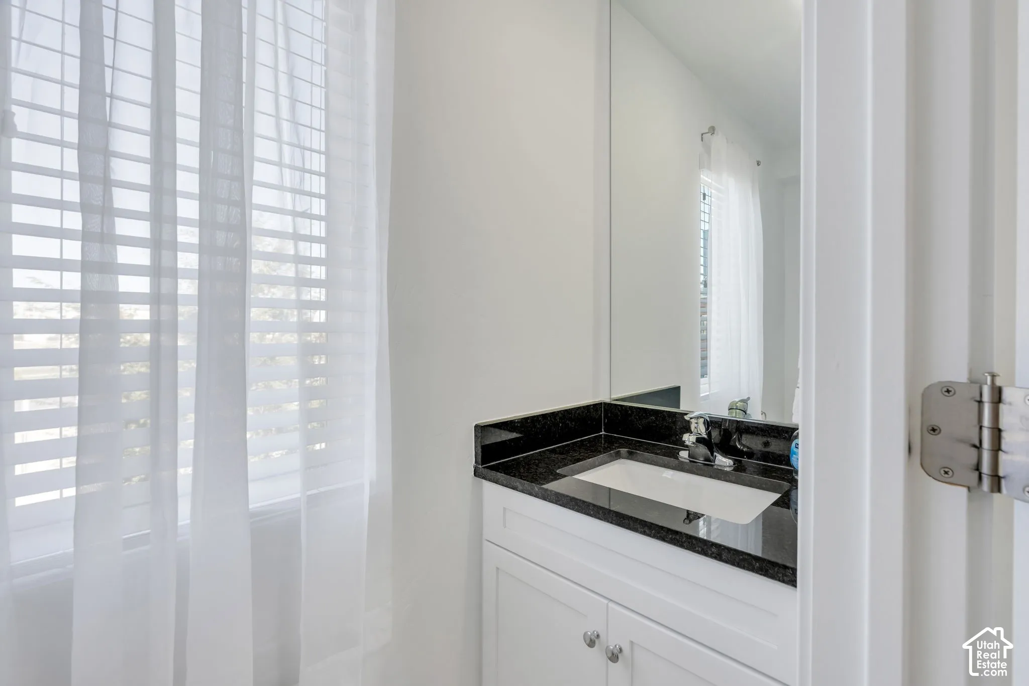 White vanity with cabinet storage, integrated sink, black countertop, and large wall-mounted mirror