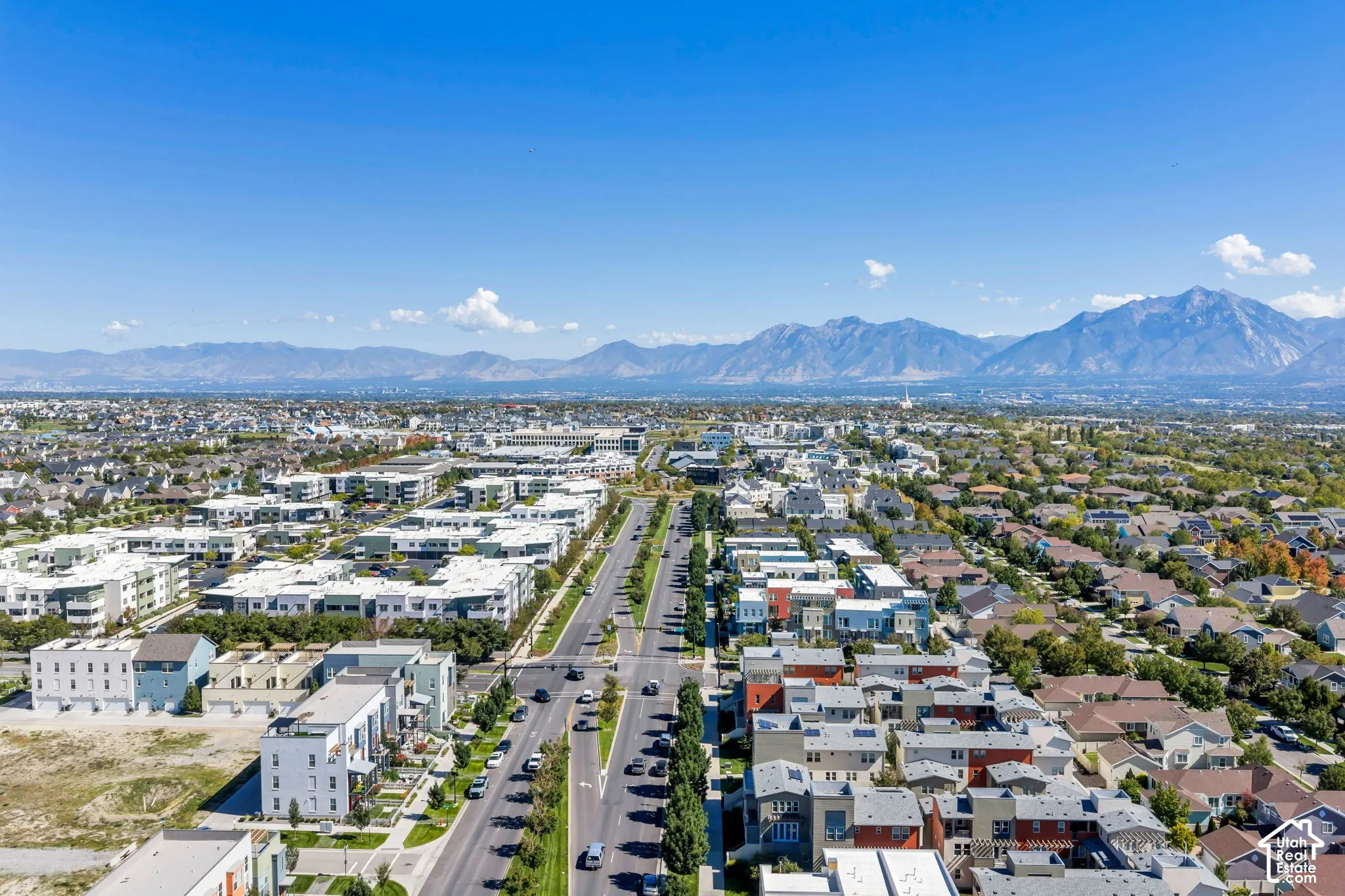 Expansive residential area with a prominent paved road, mature street trees, and a mountain range backdrop