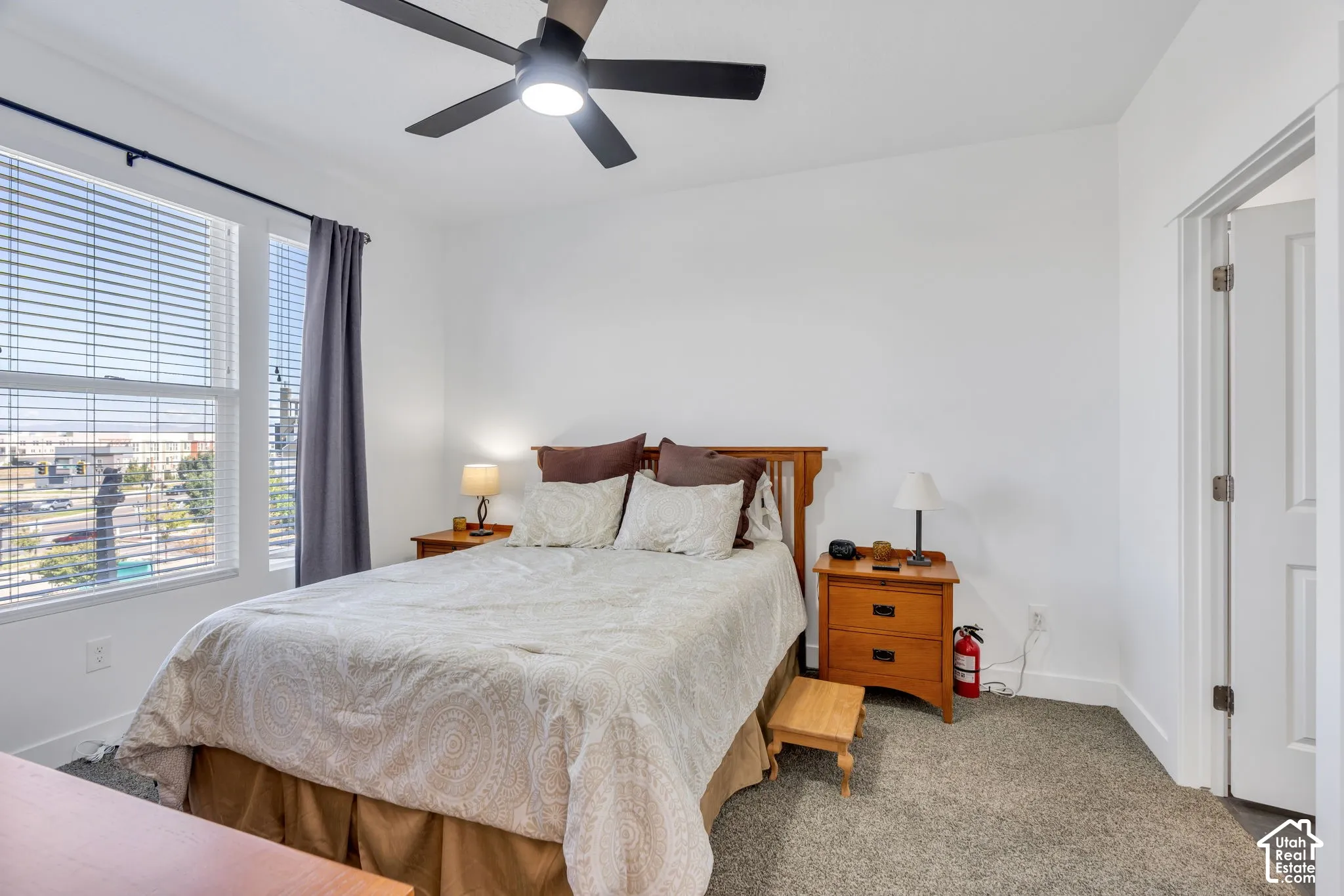 Bright room featuring a ceiling fan with integrated lighting, large windows with blinds, and textured carpeting